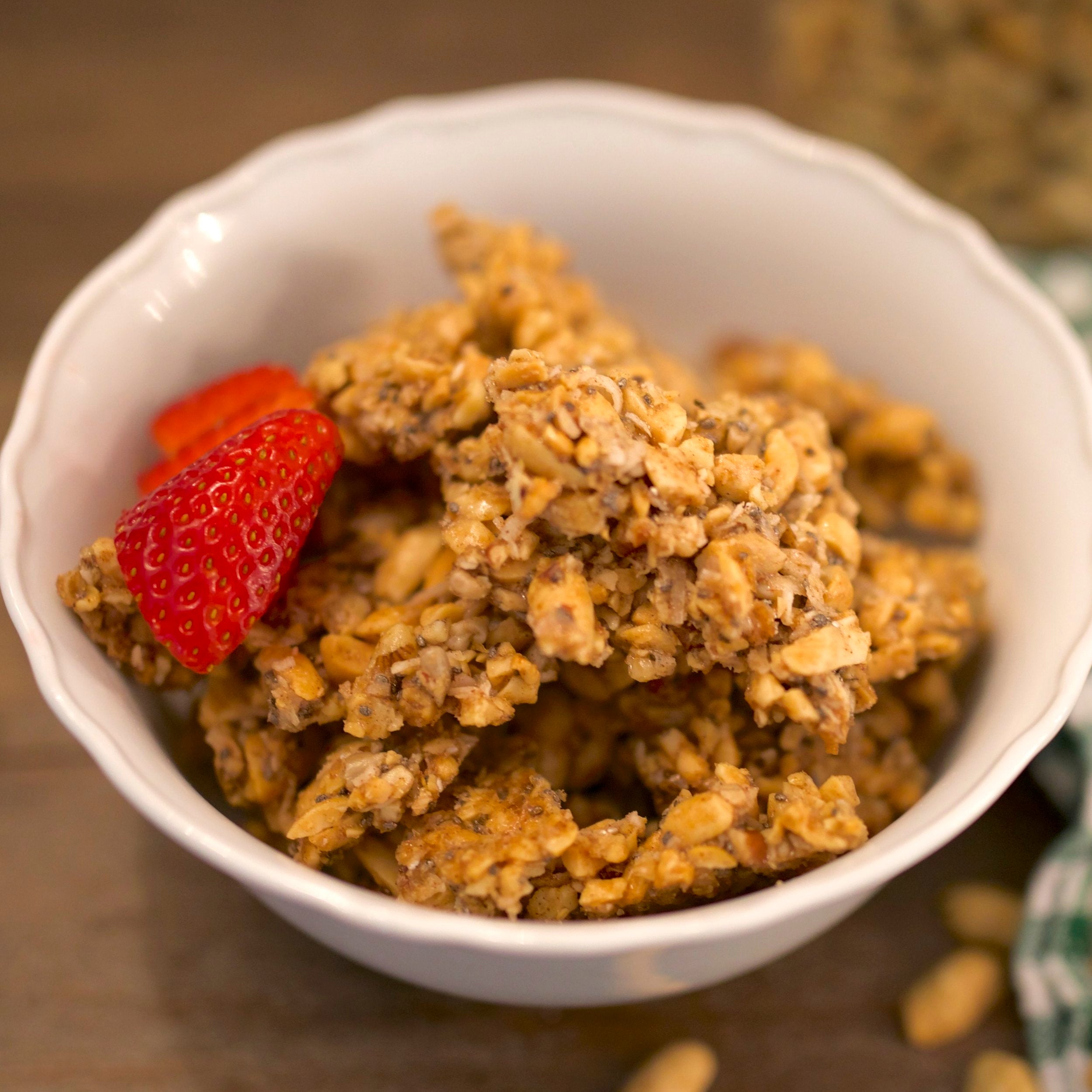 Grain-free peanut brittle granola in white bowl with strawberries