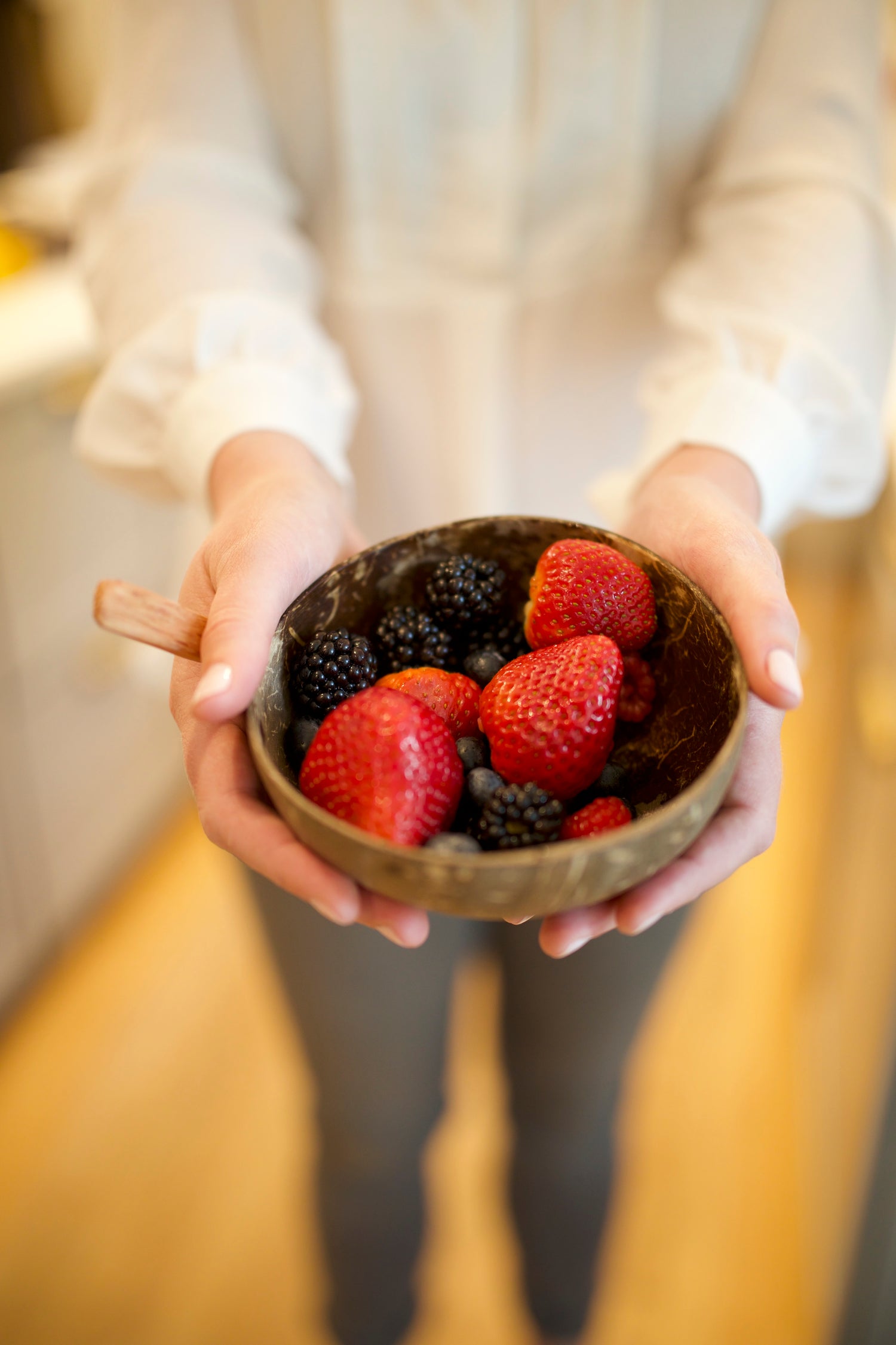 Person holding a small wooden bowl filled with strawberries and blackberries.
