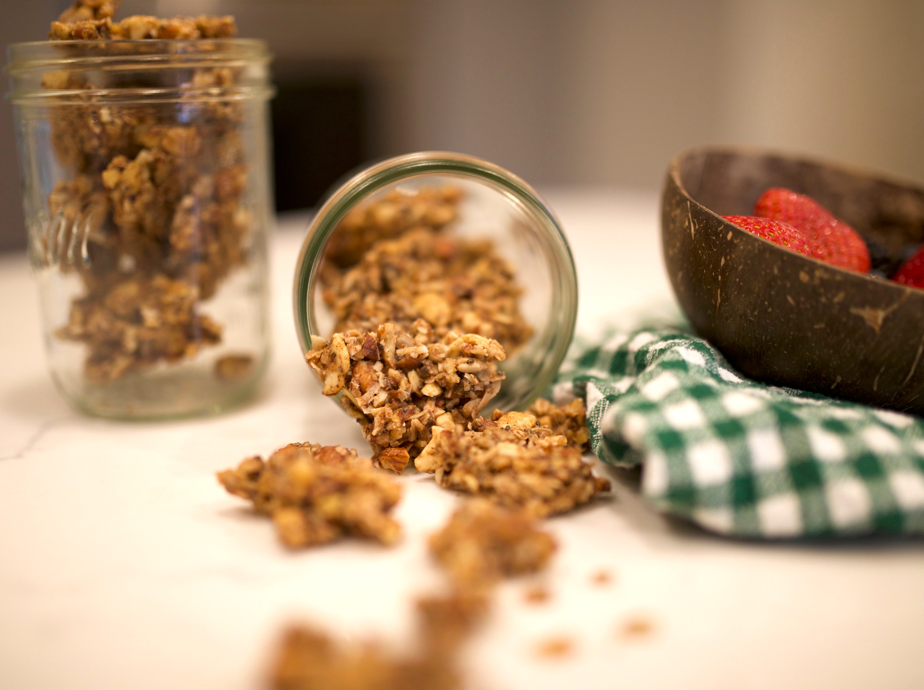 Glass jars with granola on a table with a coconut shell and checkered cloth.